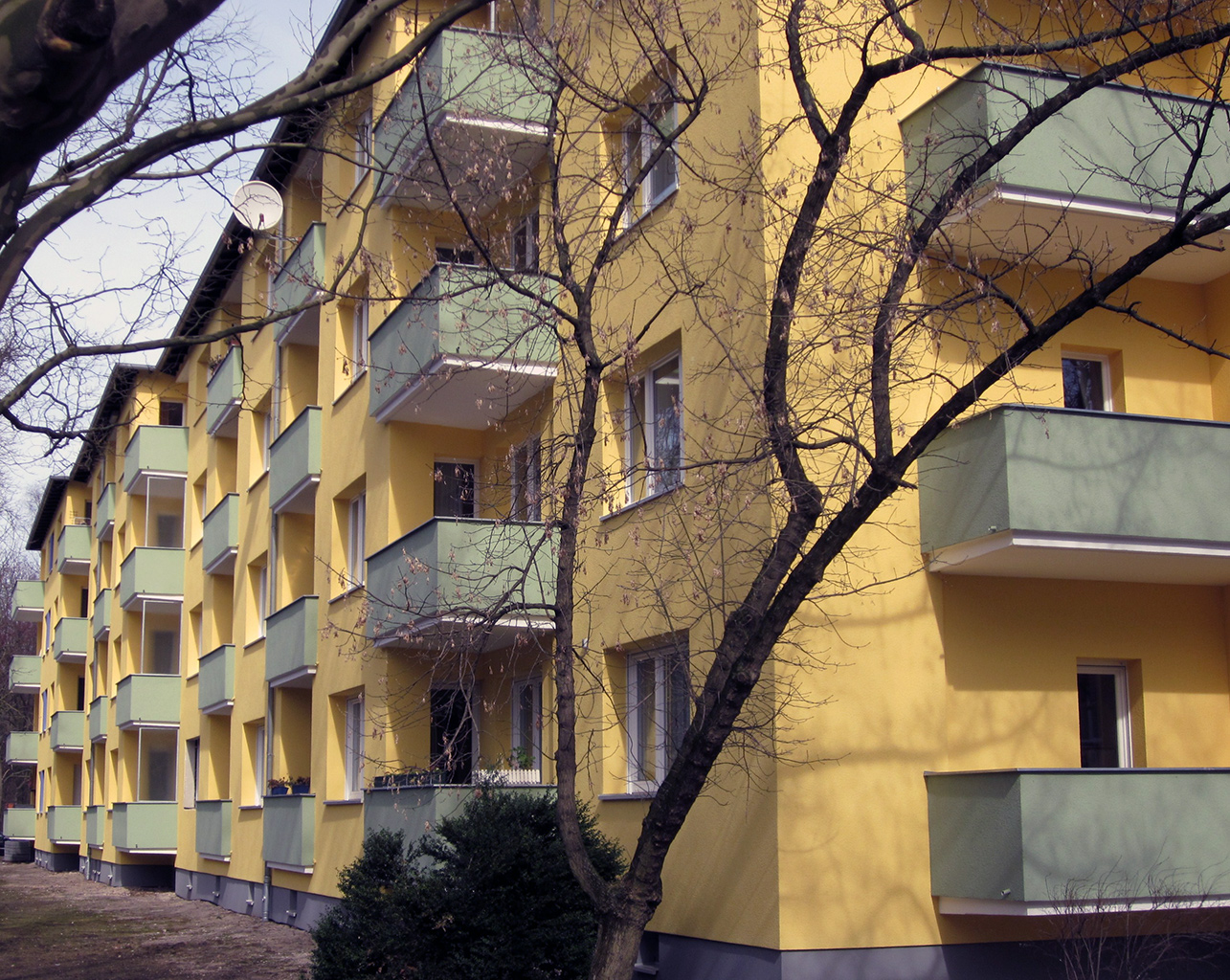 Gelbes Plattenbau-Wohngebäude mit grünen Balkonen