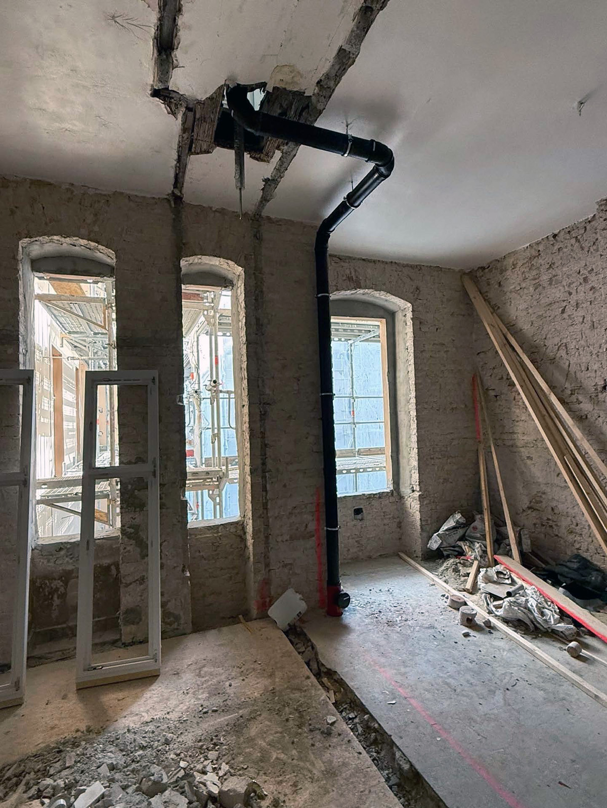 Sanierungsbaustelle mit freiliegendem Mauerwerk und schwarzem Abwasserrohr